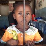 Small child holding a banana behind a bar